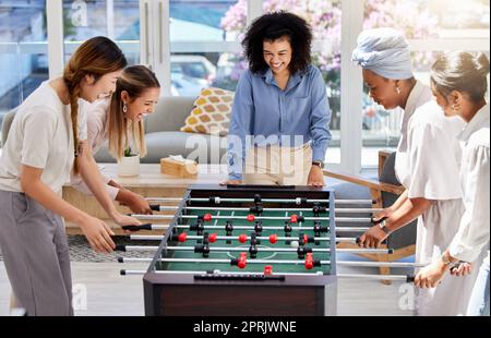 Calcio balilla o calcio, mentre le donne d'ufficio giocano insieme a una divertente partita di foosball durante la pausa pranzo al lavoro. Intrattenimento, amici felici e donne in una gara amichevole per godersi il tempo libero Foto Stock