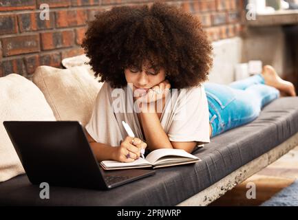 Istruzione, apprendimento e scrittura con una studentessa che studia online con il suo laptop su un divano nel suo salotto di casa. Studio, crescita e sviluppo con una studentessa che prende appunti per un esame Foto Stock