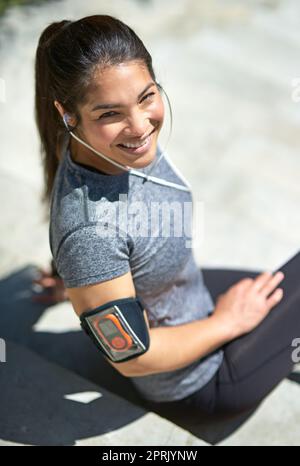 Le endorfine stanno calciando dentro. Una giovane donna sportiva che ascolta la musica mentre si siede fuori. Foto Stock