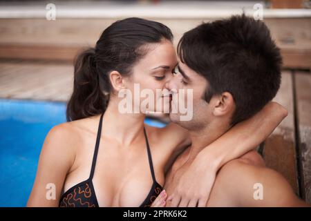 Riscaldamento in piscina. una giovane coppia attraente che condivide un bacio in piscina Foto Stock