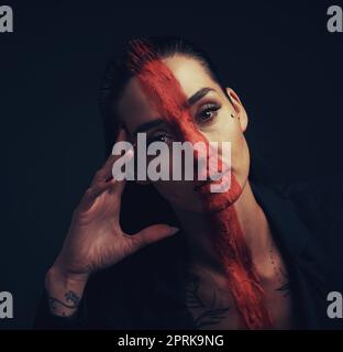 Non vivere la vita secondo le aspettative di tutti gli elses. Studio shot di una giovane donna che posa con vernice sul suo viso su uno sfondo nero Foto Stock