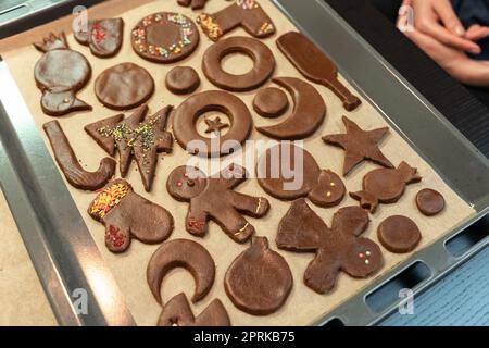 Biscotti di Natale e Capodanno di forme diverse nel processo di decorazione con un multi-colore spruzzando su una teglia da forno. Foto Stock