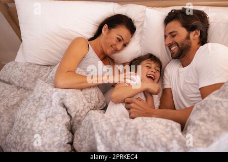 Vuole sempre essere vicino alla mamma e al papà. una giovane famiglia a letto insieme Foto Stock