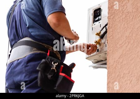Tecnico maschile professionale che ripara aria condizionata moderna all'aperto. Primo piano di un uomo che controlla, ripara o installa l'unità di aria condizionata esterna Foto Stock