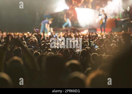 Tutti gli occhi fissi sul palco. Ripresa con la vista posteriore di un pubblico pieno di spettatori che guardano un grande atto musicale con le mani sollevate Foto Stock