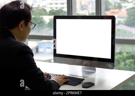 Senior manager asiatico in tuta nera sedersi alla scrivania in ufficio digitando sulla tastiera del computer con schermo bianco. Foto Stock