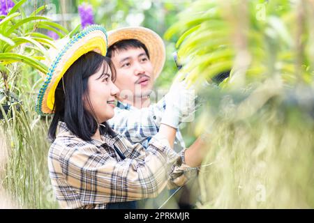 Giovane coppia agricoltori che controllano la loro fattoria di giardinaggio orchidee, donna e uomo controllare la qualità del fiore orchidea ingrandendo la lente insieme e prendere appunti Foto Stock