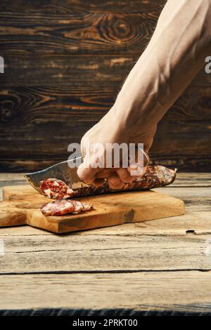 A mano con coltello tagliare salsiccia di maiale affumicata su fette di tagliere di legno Foto Stock