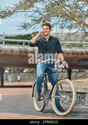 Il mondo intero alle tue ruote. un giovane studente maschio che usa il suo cellulare mentre pedalava nel campus Foto Stock