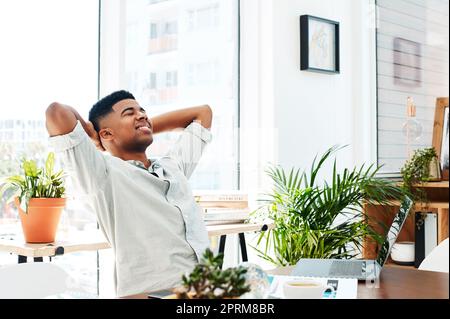 Quando lavorate duro meritate ogni ricompensa. un giovane uomo d'affari che si rilassa alla sua scrivania in un ufficio moderno Foto Stock