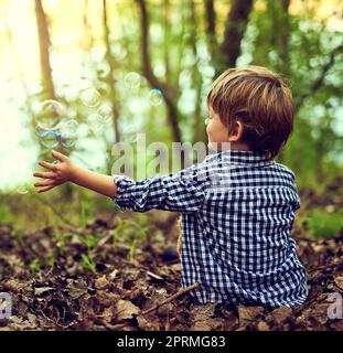 Galleggiando sul loro viaggio nel cielo, un ragazzino che gioca con le bollicine mentre si siede da solo nella foresta. Foto Stock