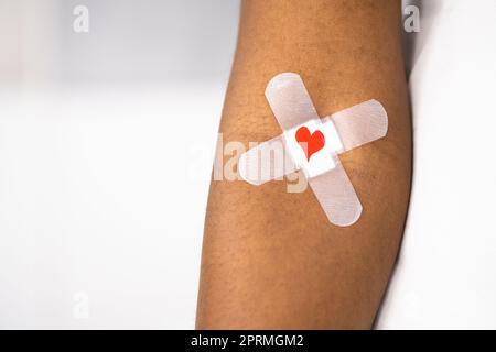 Concetto di donazione di sangue. Donatore afroamericano con aiuto di banda e cuore Foto Stock