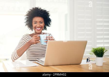 Non posso iniziare senza prima avere una buona cuppa. Ritratto di una giovane donna che beve caffè mentre lavora sul suo notebook a casa. Foto Stock