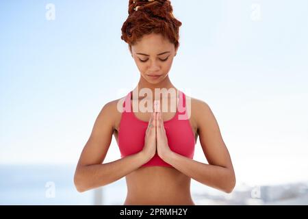 Stare in equilibrio attraverso la meditazione. Una giovane donna medita mentre fa yoga fuori in una giornata di sole. Foto Stock