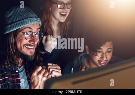 Il lavoro duro paga sempre. Un team di affari che guarda uno schermo del computer insieme durante un turno di notte al lavoro. Foto Stock