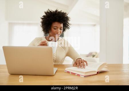 Non ha appena letto. Studia. Un giovane attraente che usa il suo laptop, legge un libro e beve un caffè a casa. Foto Stock