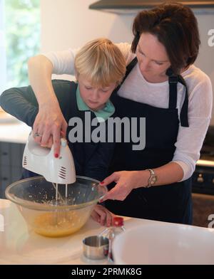 Non siete mai troppo giovani per imparare a cuocere in forno, una madre che insegna al suo bambino come cuocere in cucina a casa. Foto Stock