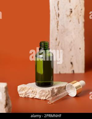 Flacone contagocce verde aperto su pietra beige su primo piano rosso, mockup cosmetico Foto Stock