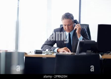 La gestione richiede abilità e pazienza. Un uomo d'affari senior che prende una chiamata alla sua scrivania. Foto Stock