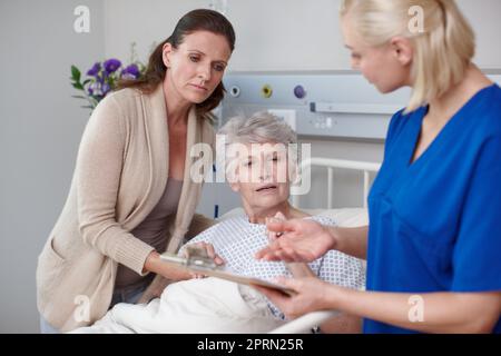 Che cosa ci dici tu. Una figlia e sua madre che guardano la forma medica che viene loro mostrata da una giovane infermiera. Foto Stock