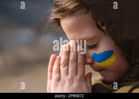 Il ragazzo ucraino chiuse gli occhi e pregava per fermare la guerra in Ucraina. Foto Stock