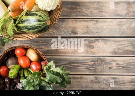 Due cestini in vimini con diverse verdure fresche sulla tavola di legno grigio, vista dall'alto. Ciotole piene di raccolto maturo. Concetto di alimentazione o di dieta sana. Piano Foto Stock