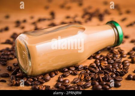 Caffè latte in bottiglia di vetro e caffè in grani sul tavolo di legno. Foto Stock