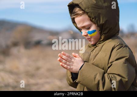 Il ragazzo ucraino chiuse gli occhi e pregava per fermare la guerra in Ucraina. Foto Stock