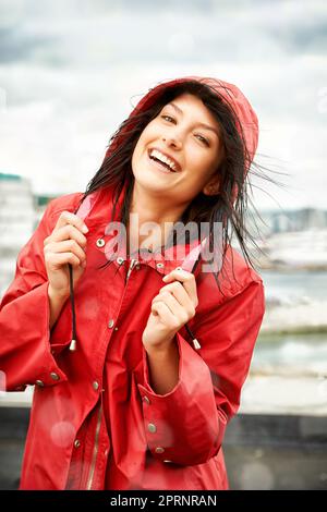 La pioggia non la disturba. Bella giovane donna sorridente mentre indossa un impermeabile rosso - ritratto Foto Stock