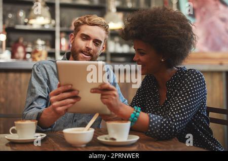 OH, WOW, puoi mandarmi questo. Una giovane coppia che usa un tablet digitale insieme in una data di caffè. Foto Stock