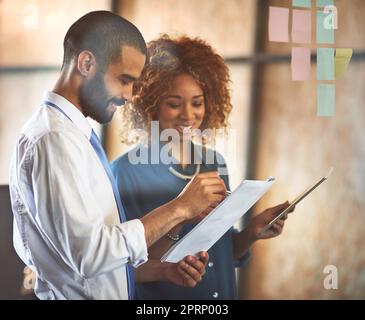 Imprenditori che fanno quello che fanno meglio. Due giovani professionisti che fanno il brainstorming con note appiccicose su una parete di vetro in un ufficio. Foto Stock