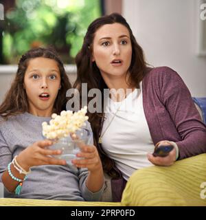 OMG. Una madre e una figlia seduti sul divano del loro soggiorno guardando un film e mangiando popcorn. Foto Stock