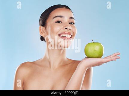 Salute, cibo e dieta di mela con la donna felice che tiene la frutta su sfondo blu. Ritratto di una giovane donna eccitata dalla perdita di peso e dalla nutrizione, mostrando i benefici di uno stile di vita sano ed equilibrato Foto Stock