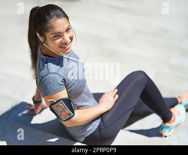 L'esercizio fisico mi fa sentire grande. Una giovane donna sportiva che ascolta la musica mentre si siede sui gradini all'aperto. Foto Stock