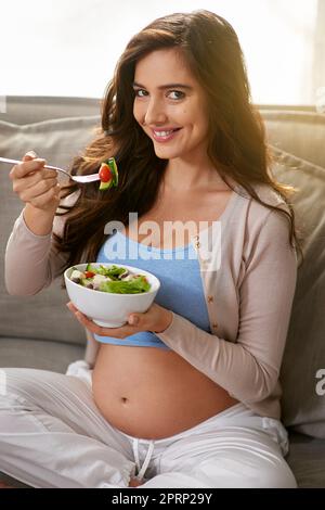 Il mio bambino lo ama quando mangio cibo biologico. Una donna incinta che mangia un'insalata sana a casa. Foto Stock