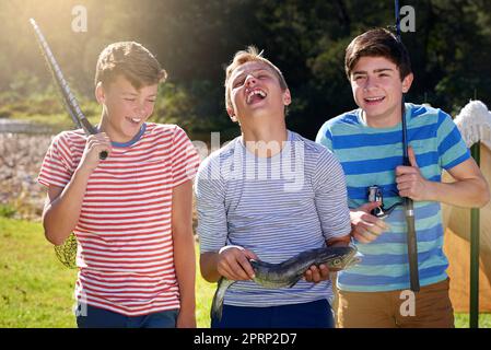 Theres qualcosa di pesce che sta succedendo qui... tre ragazzi che ridono mentre si levano in piedi con il pesce che hanno catturato. Foto Stock