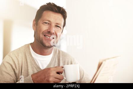 Recuperare le notizie sul caffè. Ritratto corto di un uomo che beve caffè mentre legge la carta a casa. Foto Stock