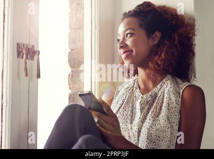 Quei testi che ti fanno sentire amato...una giovane donna che usa il suo cellulare mentre si siede accanto a una finestra. Foto Stock