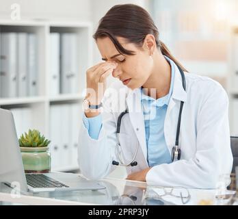 Stress, depressione e medico donna stanca che soffre di mal di testa o di salute mentale mentre si siede in un ufficio con un computer portatile. Frustrato, turbato e sovraccaricato di assistenza sanitaria o operatore medico in ospedale Foto Stock