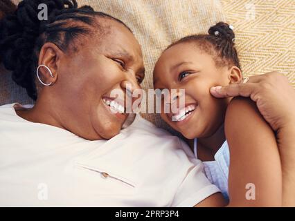 Felice, sorriso e famiglia di una nonna nera e di un bambino felicemente rilassato e sdraiato su un letto a casa. Nonna africana anziana e bambina gioiosa, amorosa e sorridente insieme in camera da letto Foto Stock