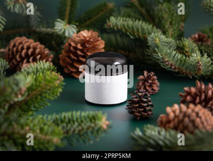 Vaso di vetro marrone vicino a rami di abete e coni di pino su primo piano verde scuro. Modello di imballaggio del marchio. Foto Stock
