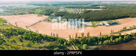 Vista aerea del granaio, del complesso di essiccazione dei cereali, del grano commerciale o del silo seme nel paesaggio rurale di Sunny Spring. Essiccatore per mais Silos, Inland Grain Terminal, elevatori per cereali in piedi in Un campo. Panorama Foto Stock