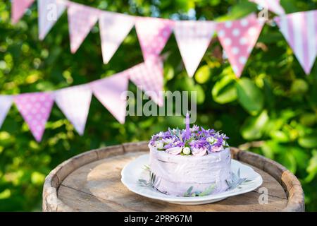 Bellissima torta bento con viola, veri peri, fiori di matthiola con foglie verdi, candele nella torta sullo sfondo di bandiere rosa. Compleanno. Foto orizzontale. Foto Stock