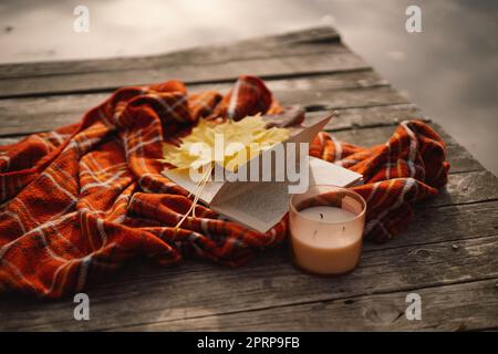 Libro aperto con candela e bouquet di foglie autunnali con un plaid su uno sfondo di legno Foto Stock