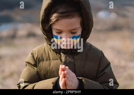 Il ragazzo ucraino chiuse gli occhi e pregava per fermare la guerra in Ucraina. Foto Stock