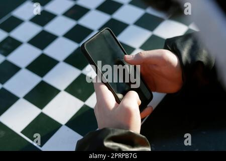 le mani del giovane uomo che tiene il telefono delle cellule sulla scacchiera Foto Stock