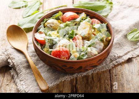 Insalata fatta in casa di uova sode, patate, pomodori, cipolle e sorrel, spinaci con condimento a base di panna in un recipiente su un tavolo di legno. Orizzontale Foto Stock