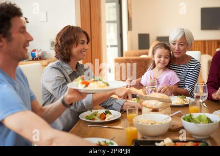 Tutti si tuffano dentro. Una famiglia multi generazionale che ha un pasto insieme intorno ad un tavolo da pranzo. Foto Stock