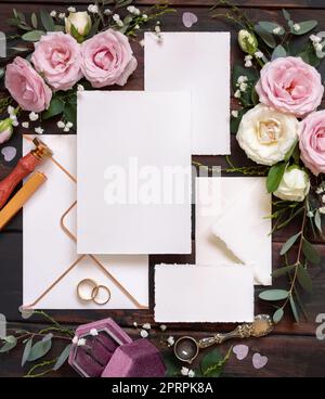 Cartoline e busta tra rose rosa e crema con vista dall'alto in legno marrone, mockup nuziale Foto Stock