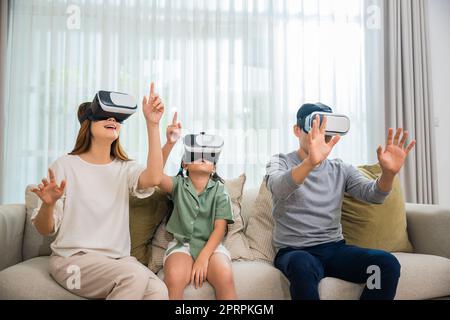 Le famiglie asiatiche indossano occhiali vr seduti sul divano del soggiorno Foto Stock